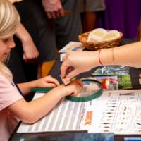 child getting a stamp on her hand from another student presenter at their exhibit table